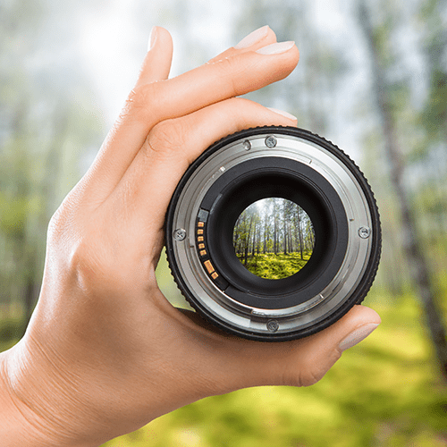 Mão segurando uma lente de máquina fotográfica com o foco na paisagem atrás